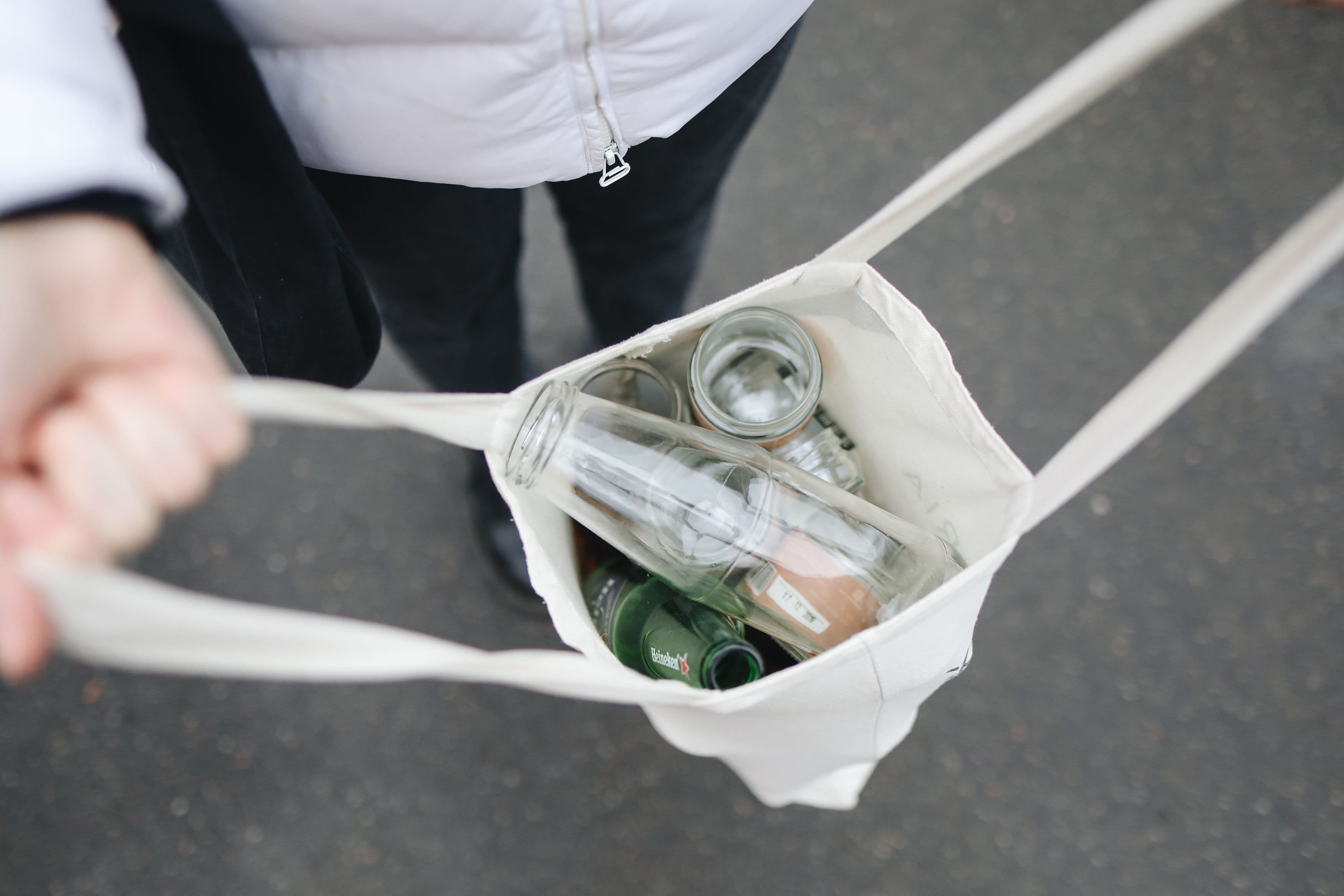 Person carrying a canvas tote bag filled with glass bottles for recycling