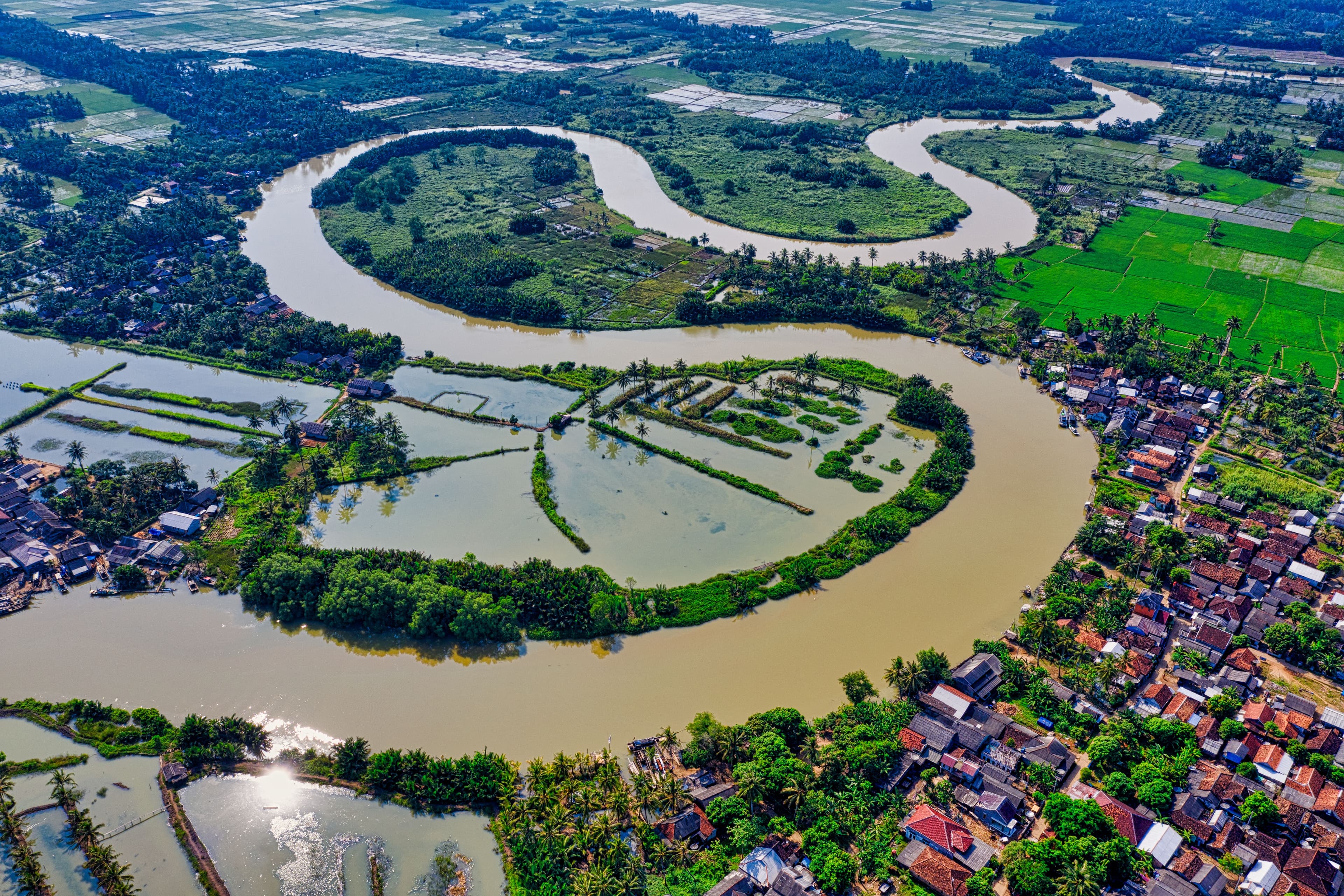 Aerial view of a winding river delta with rice paddies and a riverside village